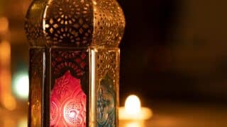 An Arab lantern with colored decorated glass that emits light in a dark background.