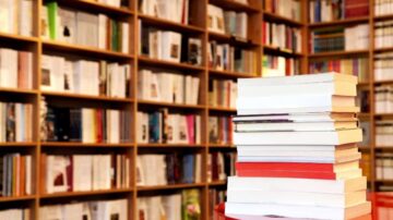 كتب مرتبة على طاولة مع خلفية مكونة من رفوف مليئة بالكتب. تظهر الكتب بألوان وأحجام متنوعة، مما يعكس تنوع المحتوى الأدبي.