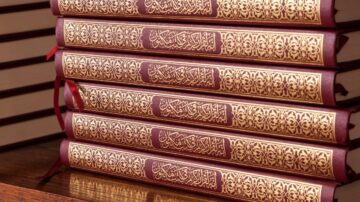 كتب دينية مزخرفة باللون البني، مع زخارف ذهبية على الغلاف، مرتبة بشكل عمودي على سطح خشبي.