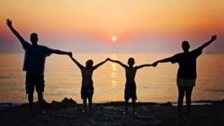 Four people hold their hands on the beach at sunset over the sea.