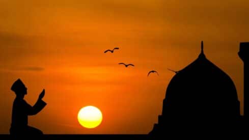 Someone calls at sunset with the shadows of a mosque and birds on the horizon.