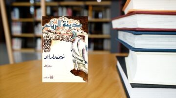 غلاف كتاب يظهر عنوان "مجنون ليلى" مع رسم تقليدي لرجل. الكتاب موضوع على طاولة خشبية بالقرب من مجموعة من الكتب في مكتبة.