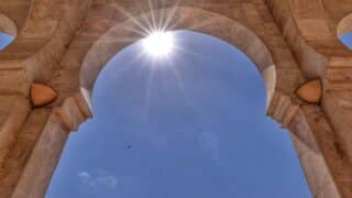 An architectural stone arch under a clear blue sky and the light of the sun through it