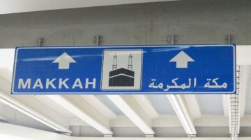 علامة توجيه زرقاء تشير إلى مكة المكرمة، تحتوي على صورة الكعبة، مع نص باللغة العربية والإنجليزية.