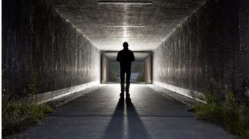 شخص يسير في نفق مظلم، مع ضوء يظهر في نهاية النفق، مما يخلق تبايناً بين الظلام والنور. يبرز الشكل البشري في الظل، مما يعكس شعوراً بالغموض والاستكشاف.