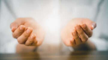 يدان مفتوحتان تتوسطهما ضوء ساطع، تعبر عن الاحتواء والتركيز. الخلفية بسيطة، مما يبرز اليدين بشكل واضح.