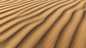 نمط من الكثبان الرملية يعكس أشعة الشمس، يظهر تفاصيل الموجات الرملية بلون ذهبي دافئ، يعبر عن جمال الطبيعة الصحراوية.