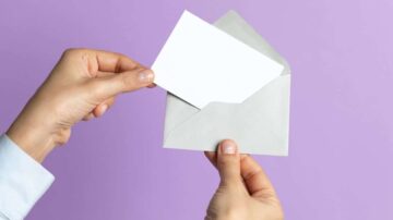 يد تحتوي على ظرف رمادي مع بطاقة بيضاء تُسحب منه، والخلفية بنفسجية.