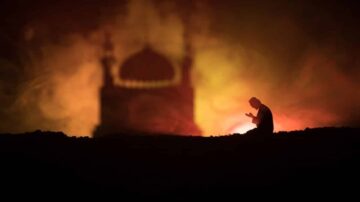 شخص يجلس في وضعية الصلاة مع خلفية غامضة لمسجد مضاء بألوان دافئة تعكس أجواء روحانية.