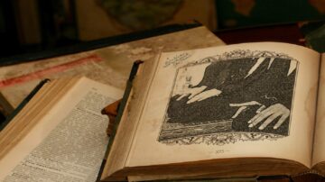 كتاب قديم مفتوح على صفحة تحتوي على رسم توضيحي ليدين تعملان على سطح. تظهر كتب أخرى حوله، مع خلفية غير واضحة.