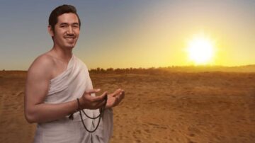 رجل يرتدي الإحرام يقف في الصحراء عند شروق الشمس، مبتسمًا ويحمل سبحة في يده. تعكس الصورة أجواء الروحانية والتأمل في بيئة طبيعية.