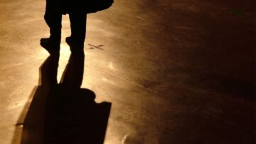 ظل شخص يقف على أرضية لامعة تحت إضاءة خافتة، مما يخلق تأثيرًا دراميًا.