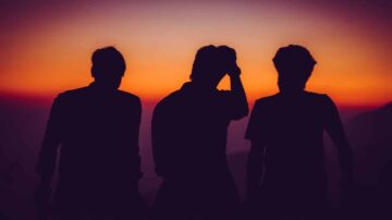 ثلاثة أشخاص يقفون في ظلال عند غروب الشمس، مع سماء ملونة بألوان دافئة. يشكل الأشخاص Silhouette بينما يتداخلون مع المنظر الطبيعي.