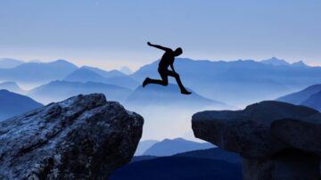 شخص يقفز بين صخرتين على خلفية جبال ضبابية، مما يبرز روح المغامرة والتحدي. منظر طبيعي يثير الإلهام ويظهر جمال الطبيعة.