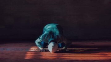 شخص يؤدي السجود في مسجد، يرتدي ملابس تقليدية، مع إضاءة خافتة وظلال تعكس روحانية اللحظة.