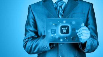 رجل يرتدي بدلة رسمية يحمل جهاز لوحي يظهر أيقونات تسوق زرقاء، مما يعكس مفهوم التجارة الإلكترونية.