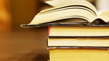 كتب مكدسة بشكل مرتب، مع كتاب مفتوح في الأعلى. يظهر الغلاف العلوي للكتاب المفتوح وأطراف الكتب السفلية، مما يعكس جوًا من القراءة والتعلم.