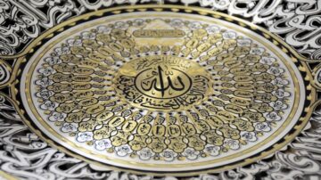 تصميم زخرفي دائري يتضمن كتابة "الله" بالخط العربي، محاط بزخارف دقيقة وأشكال هندسية باللونين الأسود والذهبي. يتضمن النقش عبارات دينية وأشكال مزخرفة تضيف لمسة فنية.