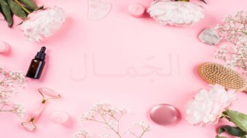 خلفية وردية تحتوي على زهور بيضاء، زيوت تجميل، حجر جاد، فرشاة شعر، ومكعبات شمع صغيرة، مما يخلق مظهرًا جماليًا مريحًا.