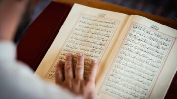 رجل يقرأ القرآن الكريم بيد واحدة، مع التركيز على النصوص العربية والتفاصيل الفنية للصفحات.