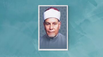 صورة لرجل مسن يرتدي عمامة بيضاء وقبعة حمراء، بزي تقليدي رمادي. تظهر ملامحه بوضوح مع خلفية ملونة.