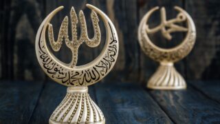 Islamic ornament with "Allah" in gem-studded Arabic calligraphy on a decorative base.