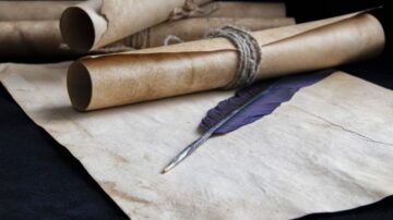 لفافة ورقية قديمة مع ريشة حبر على ورقة مسطحة. تظهر الخلفية قطع من ورق ملفوف ومربوط بخيط، مما يضيف لمسة تاريخية.