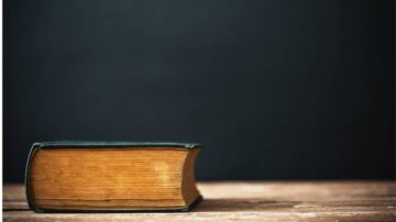 كتاب قديم مغلق على طاولة خشبية، مع خلفية داكنة. يظهر تفاصيل الحواف والتجاعيد على الصفحات.