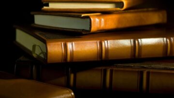 كتب جلدية ملونة مكدسة فوق بعضها البعض، مع إضاءة خفيفة تبرز تفاصيل الغلاف والملمس.