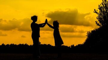 امرأة وطفل يقفان في silhouette تحت سماء صفراء مع غيوم، يتبادلان لمس الأيدي، مما يعكس لحظة عاطفية وارتباط عائلي.