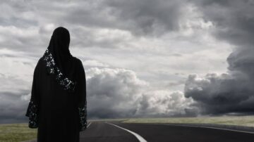 امرأة ترتدي عباءة سوداء تقف على جانب طريق خالي تحت سماء غائمة، تعكس الأجواء المشحونة والتفكير العميق.