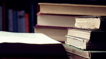 كتب قديمة وحديثة موضوعة بشكل عشوائي على طاولة، مع التركيز على تفاصيل الصفحات والتجاعيد على الغلاف.