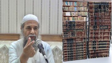 رجل يتحدث في جلسة علمية مع ميكروفون، خلفه مكتبة تحتوي على مجموعة من الكتب الإسلامية بالخط العربي، تعكس أهمية التعليم والمعرفة في الثقافة الإسلامية.