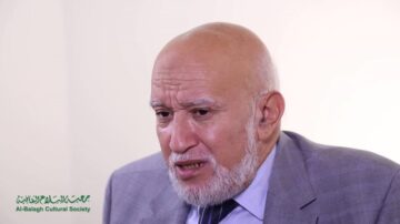 رجل مسن ذو لحية رمادية يتحدث بجدية، يرتدي بدلة رمادية وقميص أبيض، يظهر في خلفية بسيطة. شعار جمعية البلاغ الثقافية موجود في الزاوية السفلية اليسرى.