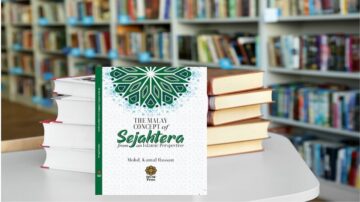 كتاب "مفهوم السيادة الماليزي من منظور إسلامي" لمحمد كامل حسن، موضوع على طاولة بيضاء، مع كتب مكدسة في الخلفية في مكتبة.