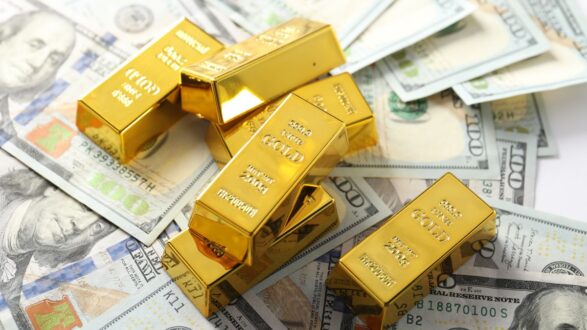 سبائك ذهبية موضوعة على أوراق نقدية من فئة المئة دولار، تعكس قيمة الذهب والمال.