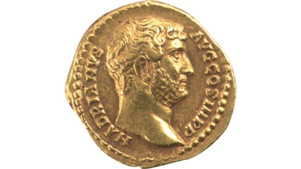 عملة ذهبية قديمة تعود للإمبراطور هادريان، تظهر وجهه بملامح واضحة، مع تفاصيل دقيقة للشعر واللحية، محاطة بحواف مزخرفة.