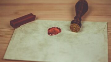 ظرفية مغلقة تحمل ختم شمعي أحمر وطبعة ختم ذهبية، موضوعان على سطح خشبي.