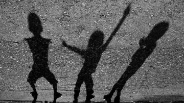 ظلال ثلاثة أطفال تلعب على سطح رملي، يظهرون بأشكال مختلفة مع تباين واضح بين الظلال.