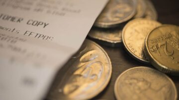 إيصال شراء ملقى بجوار عملات معدنية. الإيصال يظهر تفاصيل المعاملة والمبلغ المدفوع، بينما تظهر العملات المعدنية بأشكال وأحجام مختلفة.