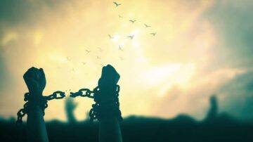 أيد مقيدة بسلاسل تتفكك تحت سماء مشمسة، مع طيور تطير في الأفق، تعبير عن الحرية والانطلاق.