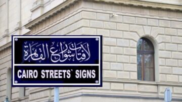 لافتة تشير إلى علامات شوارع القاهرة، مكتوبة باللغة العربية والإنجليزية، تتواجد بجوار نافذة مبنى تاريخي.