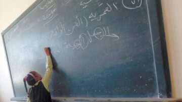 طفلة تكتب على سبورة خضراء في فصل دراسي، مع نص عربي يظهر.