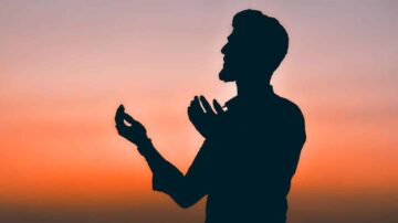 رجل يقف في وضعية الصلاة أو الدعاء في silhouette أمام غروب الشمس، مع ألوان دافئة في السماء.