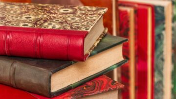 كتب ملونة متراكمة، تشمل جلدية حمراء وسوداء، مع تصميمات زخرفية على الأغلفة. تعكس الصورة جمال الكتب القديمة وتنوعها.