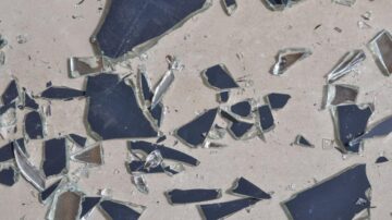 شظايا زجاج مكسور متناثرة على سطح أملس. تعكس الأجزاء اللامعة الضوء وتظهر تفاصيل الزوايا الحادة.