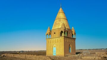 برج ذهبي مميز في منطقة صحراوية تحت سماء زرقاء صافية، مع تفاصيل معمارية تقليدية، محاط بمساحات من الأرض الجافة.