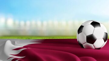 كرة قدم سوداء وبيضاء على علم قطر، مع خلفية ضبابية لميدان كرة القدم.