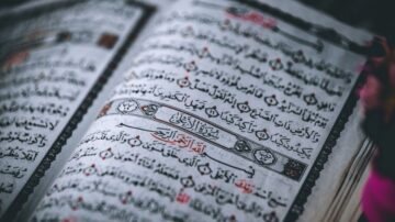 صفحة من القرآن الكريم تظهر نصوصًا باللغة العربية مع تزيينات تقليدية. الكتاب مفتوح يظهر آيات واضحة بخط عربي جميل.
