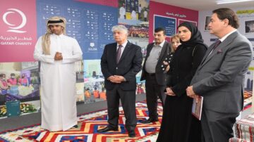 زيارة لمعرض قطر الخيرية، حيث يقف الحضور أمام لوحات توضح إنجازات الجمعية. يظهر في الصورة أربعة أشخاص، رجل يرتدي الزي التقليدي القطري، ورجل آخر في بدلة، وامرأتان، واحدة ترتدي الحجاب والأخرى ترتدي ملابس أنيقة. يمثل المعرض جهد قطر الخيرية في تقديم المساعدات الإنسانية.